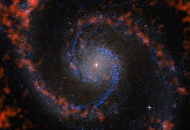 Abbildung 2: Molekül- und Gaswolken in der Whirlpool-Galaxie M 51. Die blauen Strukturen zeigen die Verteilung der Wasserstoffmoleküle in M51 an, des Rohmaterials für die Sternentstehung. Die Astronomen des PAWS-Teams haben aus diesen Daten einen Katalog von mehr als 1.500 Molekülwolken erstellt. In rot sind Wolken von atomarem Wasserstoff sichtbar. Im Hintergrund ist ein Bild der Galaxie im sichtbaren Licht zu sehen, aufgenommen mit dem Weltraumteleskop Hubble. Darüber ist in blau die CO(1-0)-Strahlung der Kohlenstoffmonoxid-Moleküle gezeigt, die für die PAWS-Studie mit den Millimeterteleskopen des Institut de Radioastronomie Millimétrique aufgenommen wurden; da Kohlenstoffmonoxid- und Wasserstoffmoleküle zusammen auftreten, zeigt diese Strahlung die Verteilung von molekularem Wasserstoff an. Rot ist die HI-Linienemission des atomaren Gases dargestellt.