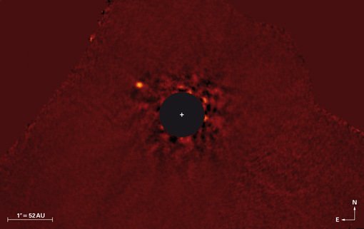 Abbildung 1: Falschfarbenes Nahinfrarotbild (3,8 Mikrometer Wellenlänge) des κ And (»Kappa Andromedae«)-Systems, aufgenommen mit dem Subaru-Teleskop auf Hawaii im Juli 2012. Der Großteil des Lichts des Muttersterns, auf den das Bild zentriert ist, wurde durch Bildverarbeitung herausgefiltert. Die Flecken rund um die Scheibe sind Resteffekte des herausgerechneten Sternenlichts. Der Super-Jupiter κ And b ist oben links deutlich zu sehen. Im Bild entspricht sein Abstand vom Mutterstern dem 1,8fachen des Abstands des Neptuns von der Sonne.
