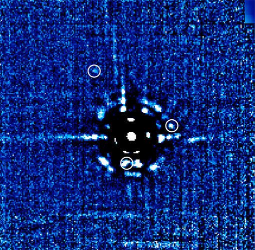 Abbildung 1: Bild des HR 8799-Planetensystems, in der Mitte: der Zentralstern HR 8799. Eine sorgfältige Untersuchung zeigt, dass es sich bei drei der Lichtflecken um Planeten handelt (durch Kreise gekennzeichnet): Bei 11 Uhr angefangen, im Uhrzeigersinn, und von außen nach innen sind das HR 8799b, HR8799c und HR8799d. Die anderen Strukturen sind Artefakte, wie sie bei einer solch schwierigen Beobachtungssituation – Stern und Planeten stehen extrem nahe beieinander, und der Stern ist einige tausend Mal heller als die Planeten – unvermeidbar sind. Der Abstand vom Stern zu HR 8799c entspricht dem 38fachen des mittleren Abstands von der Sonne zur Erde.