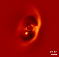 Nah-Infrarot-Aufnahme der PDS70-Scheibe aufgenommen mit dem SPHERE-Instrument. Der junge Exoplanet PDS 70 b ist deutlich als helles Signal am inneren Rand der Lücke (dunkler Bereich) zu erkennen. Die vom Zentralstern ausgehende Emission wurde ausgeblendet. Der Balken rechts unten zeigt den linearen Maßstab des Bildes in einer Entfernung von 370 Lichtjahren an.