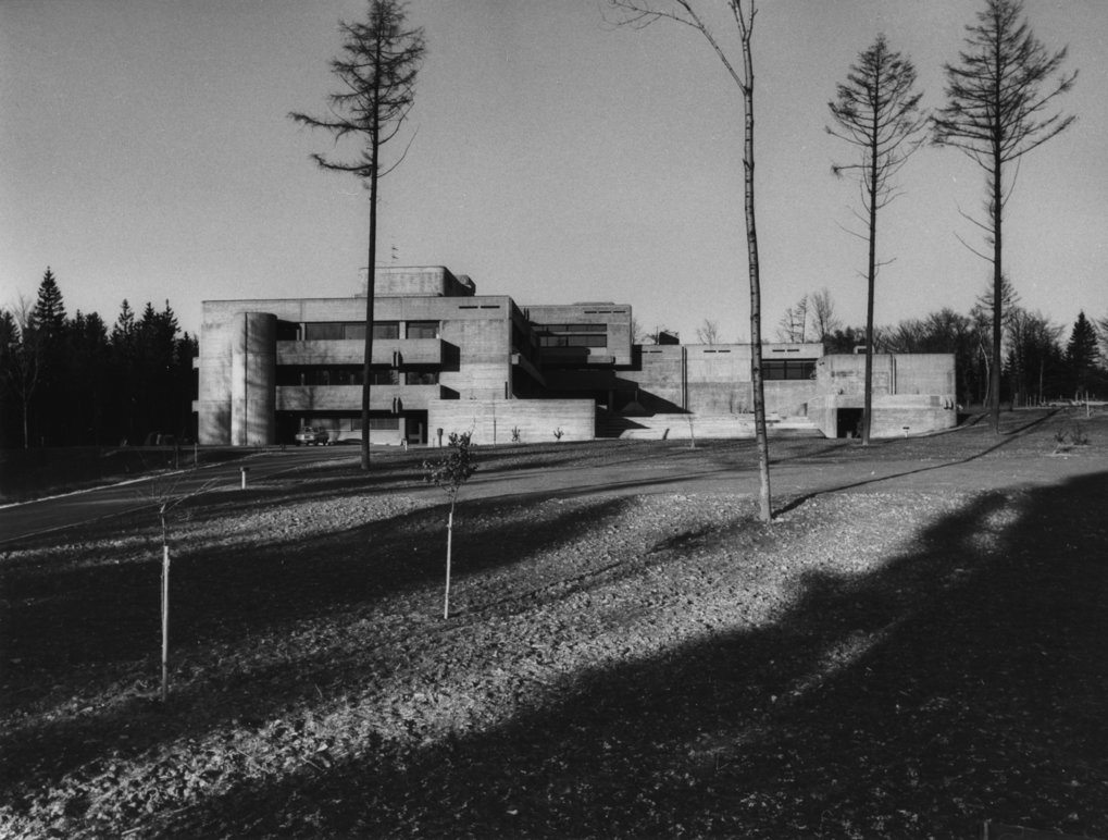 Das 1975 fertiggestellte Hauptgebäude des MPIA von Süden (vom Astrolabor aus) gesehen. Das Bild dokumentiert den ursprünglichen Zustand des Hauptgebäudes: Sichtbeton, 3 Etagen. Auf das Gebäude wurde 2005 eine weitere Etage aufgesetzt, der Beton wurde mit schützender Farbe überstrichen. © MPIA