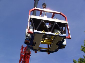 LINC-NIRVANA schwebt in luftiger Höhe in seiner roten Tragstruktur am Kran. LINC-NIRVANA schwebt in luftiger Höhe in seiner roten Tragstruktur am Kran.