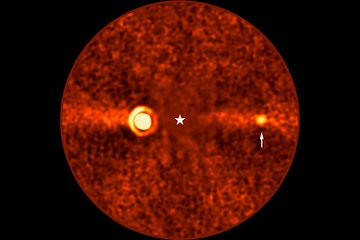 Runde, rötlich gefärbte astronomische Aufnahme mit körniger Struktur. Im Zentrum befindet sich ein weißes Sternsymbol, das die Position des Sterns Beta Pictoris markiert, der auf dem Bild nicht sichtbar ist. Links vom Zentrum ist ein auffällig leuchtender Bereich mit konzentrischen Kreisen zu sehen, ein Abbild des Exoplaneten Beta Pictoris b. Eine horizontale, helle Linie durchzieht das Bild und repräsentiert die Trümmerscheibe um den Stern. Rechts vom Zentrum hebt ein kleiner, heller Punkt, markiert durch einen weißen Pfeil, einen weiteren Exoplaneten hervor: Beta Pictoris d.