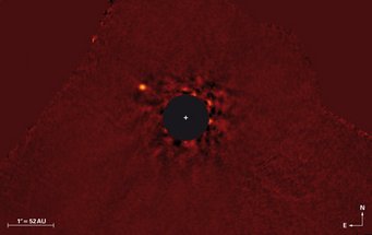 Abbildung 1: Falschfarbenes Nahinfrarotbild (3,8 Mikrometer Wellenlänge) des κ And (»Kappa Andromedae«)-Systems, aufgenommen mit dem Subaru-Teleskop auf Hawaii im Juli 2012. Der Großteil des Lichts des Muttersterns, auf den das Bild zentriert ist, wurde durch Bildverarbeitung herausgefiltert. Die Flecken rund um die Scheibe sind Resteffekte des herausgerechneten Sternenlichts. Der Super-Jupiter κ And b ist oben links deutlich zu sehen. Im Bild entspricht sein Abstand vom Mutterstern dem 1,8fachen des Abstands des Neptuns von der Sonne. Abbildung 1: Falschfarbenes Nahinfrarotbild (3,8 Mikrometer Wellenlänge) des κ And (»Kappa Andromedae«)-Systems, aufgenommen mit dem Subaru-Teleskop auf Hawaii im Juli 2012. Der Großteil des Lichts des Muttersterns, auf den das Bild zentriert ist, wurde durch Bildverarbeitung herausgefiltert. Die Flecken rund um die Scheibe sind Resteffekte des herausgerechneten Sternenlichts. Der Super-Jupiter κ And b ist oben links deutlich zu sehen. Im Bild entspricht sein Abstand vom Mutterstern dem 1,8fachen des Abstands des Neptuns von der Sonne.
