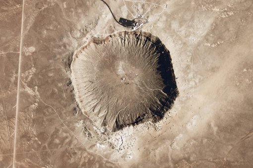 Abb. 1: Der Barringer-Krater, auch als "Meteor Crater" bekannt, in Arizona. Dieser Krater entstand vor rund 50.000 Jahren beim Einschlag eines Nickel-Eisen-Meteoriten. Am oberen Bildrand ist das Besucherzentrum zu sehen, inklusive einiger Reisebusse auf dem Parkplatz.