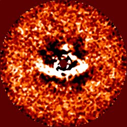 Abb. 1: Dieses Bild der HiCIAO-Kamera am SUBARU-Teleskop bietet einen Blick auf die protoplanetaren Scheibe des jungen Sterns LkCa 15. Ein Teil der Scheibe (weiss) wird vom Stern (Mitte, dunkelrot maskiert) beleuchtet und so sichtbar gemacht. Deutlich zu erkennen ist die scharf definierte Innenkante der Scheibe, wo der Leerraum in ihrer Mitte anfängt. Die Aussparung ist unsymmetrisch – sie ist links deutlich größer als rechts – und dürfte auf einen oder mehrere neugeborene Planeten zurückgehen, die dort um den Stern umlaufen. Abb. 1: Dieses Bild der HiCIAO-Kamera am SUBARU-Teleskop bietet einen Blick auf die protoplanetaren Scheibe des jungen Sterns LkCa 15. Ein Teil der Scheibe (weiss) wird vom Stern (Mitte, dunkelrot maskiert) beleuchtet und so sichtbar gemacht. Deutlich zu erkennen ist die scharf definierte Innenkante der Scheibe, wo der Leerraum in ihrer Mitte anfängt. Die Aussparung ist unsymmetrisch – sie ist links deutlich größer als rechts – und dürfte auf einen oder mehrere neugeborene Planeten zurückgehen, die dort um den Stern umlaufen.