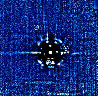 Abbildung 1: Bild des HR 8799-Planetensystems, in der Mitte: der Zentralstern HR 8799. Eine sorgfältige Untersuchung zeigt, dass es sich bei drei der Lichtflecken um Planeten handelt (durch Kreise gekennzeichnet): Bei 11 Uhr angefangen, im Uhrzeigersinn, und von außen nach innen sind das HR 8799b, HR8799c und HR8799d. Die anderen Strukturen sind Artefakte, wie sie bei einer solch schwierigen Beobachtungssituation – Stern und Planeten stehen extrem nahe beieinander, und der Stern ist einige tausend Mal heller als die Planeten – unvermeidbar sind. Der Abstand vom Stern zu HR 8799c entspricht dem 38fachen des mittleren Abstands von der Sonne zur Erde. Abbildung 1: Bild des HR 8799-Planetensystems, in der Mitte: der Zentralstern HR 8799. Eine sorgfältige Untersuchung zeigt, dass es sich bei drei der Lichtflecken um Planeten handelt (durch Kreise gekennzeichnet): Bei 11 Uhr angefangen, im Uhrzeigersinn, und von außen nach innen sind das HR 8799b, HR8799c und HR8799d. Die anderen Strukturen sind Artefakte, wie sie bei einer solch schwierigen Beobachtungssituation – Stern und Planeten stehen extrem nahe beieinander, und der Stern ist einige tausend Mal heller als die Planeten – unvermeidbar sind. Der Abstand vom Stern zu HR 8799c entspricht dem 38fachen des mittleren Abstands von der Sonne zur Erde.