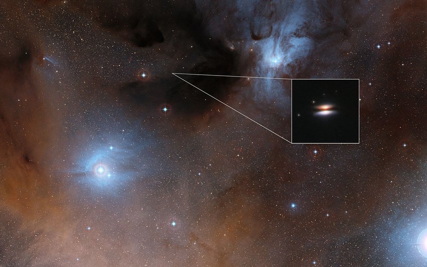 An image of Flying Saucer (2MASS J16281370-2431391) protoplanetary disk at visual wavelengths. The disk is seen nearly perfectly edge-on. The dark lane is produced by dust grains located in the center of the disk that absorbs the light from the central star. The bright symmetric cones are stellar radiation scattered by dust particles above the disk midplane. An image of Flying Saucer (2MASS J16281370-2431391) protoplanetary disk at visual wavelengths. The disk is seen nearly perfectly edge-on. The dark lane is produced by dust grains located in the center of the disk that absorbs the light from the central star. The bright symmetric cones are stellar radiation scattered by dust particles above the disk midplane.