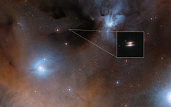 An image of Flying Saucer (2MASS J16281370-2431391) protoplanetary disk at visual wavelengths. The disk is seen nearly perfectly edge-on. The dark lane is produced by dust grains located in the center of the disk that absorbs the light from the central star. The bright symmetric cones are stellar radiation scattered by dust particles above the disk midplane.