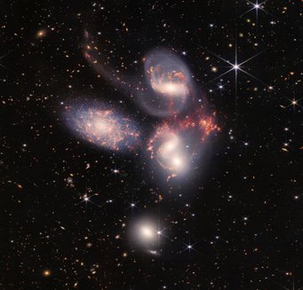 High five: Das Stephans Quintett besteht aus fünf Galaxien, die miteinander wechselwirken. Fünf Galaxien vor einem schwarzen Hintergrund, der mit hellen Punkten und Objekten übersät ist.