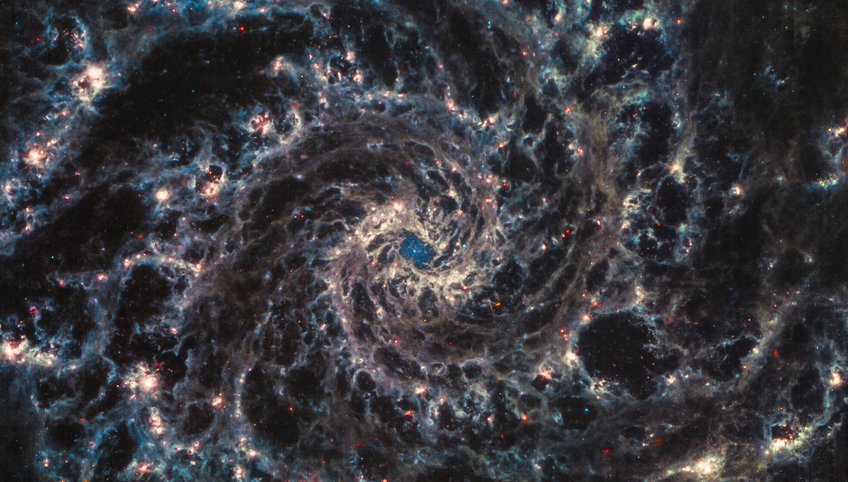 Neue JWST-Bilder geben Wissenschaftlern erstmals einen hochauflösenden Einblick in die feinen Strukturen naher Galaxien und wie diese durch die Geburt von jungen Sternen beeinflusst werden. Dieses aus drei Farben zusammengesetzte Bild zeigt NGC 628 (M 74), eine eindrucksvolle Spiralgalaxie in einer Entfernung von 32 Millionen Lichtjahren. Das Bild kombiniert MIRI-Bilder, die bei Wellenlängen von 21,0 (Rot), 11,3 (Orange), 7,7 (Cyan) und 10,0 (Graustufen) Mikrometern aufgenommen wurden. Während das galaktische Zentrum von verschlungenen Bahnen aus glühendem Staub umgeben ist, ist in seinem Kern ein unverhüllter zentraler Sternhaufen (Nuclear Star Cluster, NSC) sichtbar. Diese Daten liefern auch deutliche Hinweise auf neu entstandene Sterne in den Ausläufern aus Gas und Staub zwischen benachbarten Spiralarmen. Ein farbiges Netz, das einem Strudel mit einer zentralen Verdichtung ähnelt.