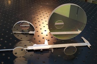 Die vier im NISP-Instrument verbauten Infrarotfilter mit Durchmessern von vier Zentimetern im Vordergrund, sowie acht und vierzehn Zentimetern im Hintergrund. Mit über 300 Gramm pro Filter sind das die größten und schwersten Infrarotfilter, die je auf einer astronomischen Weltraummission eingesetzt wurden. Die Basis aller Filter ist Quartzglas, das speziell beschichtet wird, damit jeder Filter nur Infrarotlicht bei ganz bestimmten Wellenlängen passieren lässt. Auf einer Lochplatte stehen zwei gleich große kleine kreisrunde Scheiben aufrecht nebeneinander, direkt dahinter in einer zweiten Reihe eine etwa doppelt so große und eine viermal so große Scheibe. Eine Schieblehre liegt zwischen beiden Reihen. Die Scheiben spiegeln, was sich vor ihnen befindet.