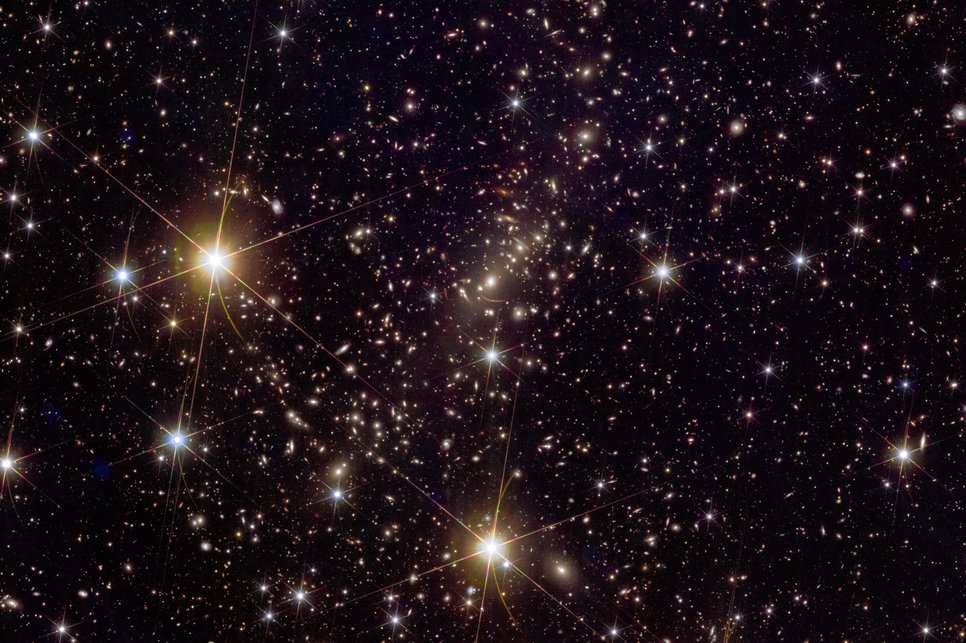 Euclid image of the galaxy cluster Abell 2390. The arc-like structures in the center (not around the bright stars!) are images of galaxies distorted by the gravitational lensing effect, which from our point of view are located far behind the cluster. The distortion of the light rays is caused by the large mass of visible and, above all, dark matter of the cluster in the foreground, which acts like a lens. Such lensing effects can provide information about the distribution of the mysterious dark matter. The image shows only a small part of the whole image taken with Euclid.