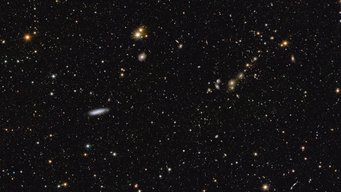 Dieses Bild zeigt einen Bereich des Mosaiks, das vom ESA-Weltraumteleskop Euclid am 15. Oktober 2024 veröffentlicht wurde. Der Bereich ist im Vergleich zum großen Mosaik zwölfmal vergrößert. In der Mitte links ist die Spiralgalaxie NGC 2188 in einer Entfernung von 25 Millionen Lichtjahren am Rande sichtbar. In der rechten oberen Ecke ist der Galaxienhaufen Abell 3381 deutlich zu erkennen, der 678 Millionen Lichtjahre von uns entfernt ist. Ein Meer von Lichtpunkten, die gleichmäßig über einen schwarzen Hintergrund verstreut sind, wobei einige hellere und bunte Punkte hervorstechen. Wenn man von links nach rechts über das Bild blickt, fällt in der linken oberen Ecke zuerst ein heller orangefarbener Stern mit sechs schwachen Zacken ins Auge. Unten rechts davon, knapp unterhalb der Bildmitte, schwebt eine dünne weiße elliptische Galaxie ins Bild. Etwas weiter rechts darüber tanzt ein Paar heller goldgelber Sterne ins Bild. Weiter rechts, im letzten Drittel des Bildes, ist eine kurze Reihe von Sternen und Galaxien zu sehen. Diese erscheint wie eine im 45-Grad-Winkel geneigte Kette, an der dunstige Galaxien in verschiedenen Gelbtönen wie Perlen an einem kosmischen Armband aufgereiht sind.