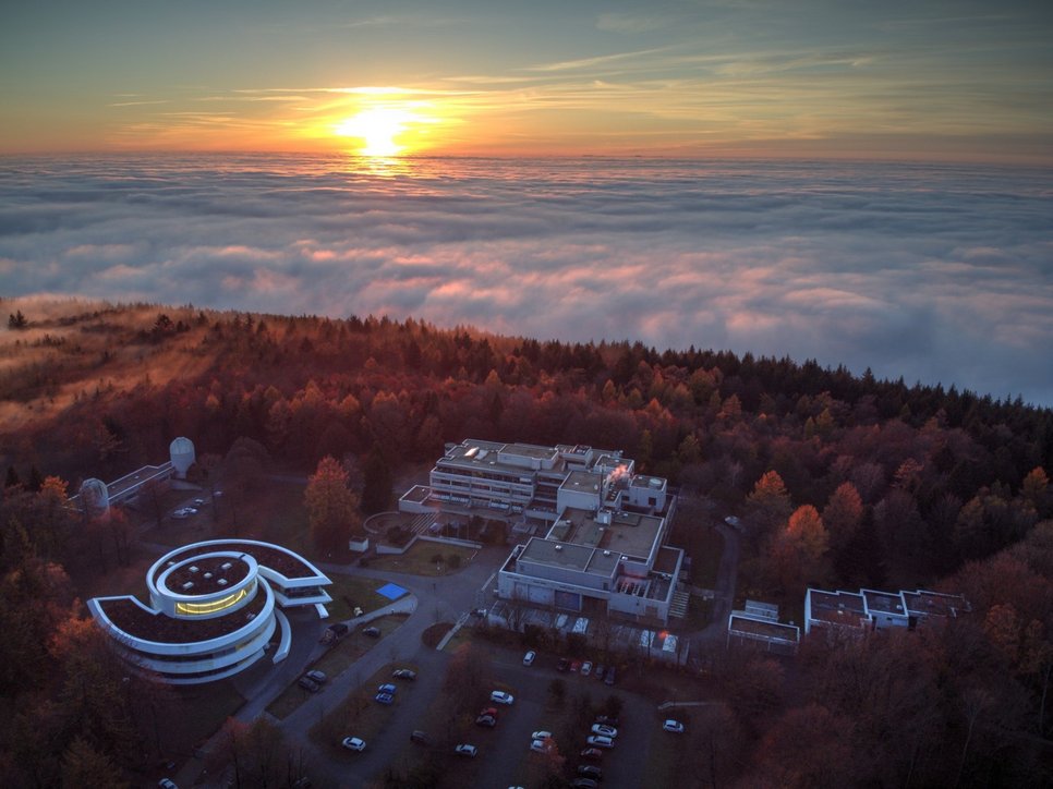 Luftbild des MPIA-Campus auf dem Königstuhl mit dem spiralförmigen Haus der Astronomie (links unten), den Teleskop-Kuppelgebäuden des Elsässer-Labors (links) und dem MPIA-Hauptgebäude (Mitte). Der Erweiterungsbau wird sich in Richtung der Kuppelgebäude an das Südende des Hauptgebäudes anschließen. 