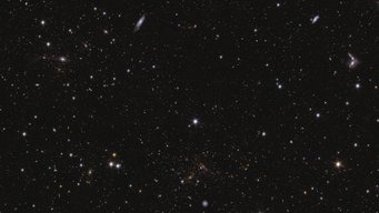 This image shows an area of Euclid’s Deep Field South. The area is zoomed in 16 times compared to the large mosaic. Many galaxies are visible in this field, all with different shapes and colours because they have different ages and distances. A sea of stars and galaxies sparkle against a black background. Several galaxies can be identified by their elongated shape and/or spiral arms. Some galaxies are seen edge-on while one prominent spiral galaxy at the bottom centre is seen face-on. At the far right, between the middle and top of the image, are some interacting galaxies. Galaxy clusters are also seen, in particular near bottom centre, where features smeared into arcs represent gravitational lensing. The brightest stars in the image have diffraction spikes.