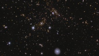 This image shows an area of Euclid’s Deep Field South. The area is zoomed in 70 times compared to the large mosaic. Various huge galaxy clusters are visible in this image, as well as intra-cluster light, and gravitational lenses. The cluster near the centre is called J041110.98-481939.3, and is located almost 6 billion light-years away.  A sea of galaxies of many different shapes and sizes, oriented in all directions and many with spiral arms visible. A large, nearby face-on spiral galaxy draws attention at the bottom centre of the image. Two bright stars in the centre and to the left are seen with prominent diffraction spikes. In between the two stars lie a lensed galaxy cluster, with arc-like smears surrounding the central bright galaxy cluster.
