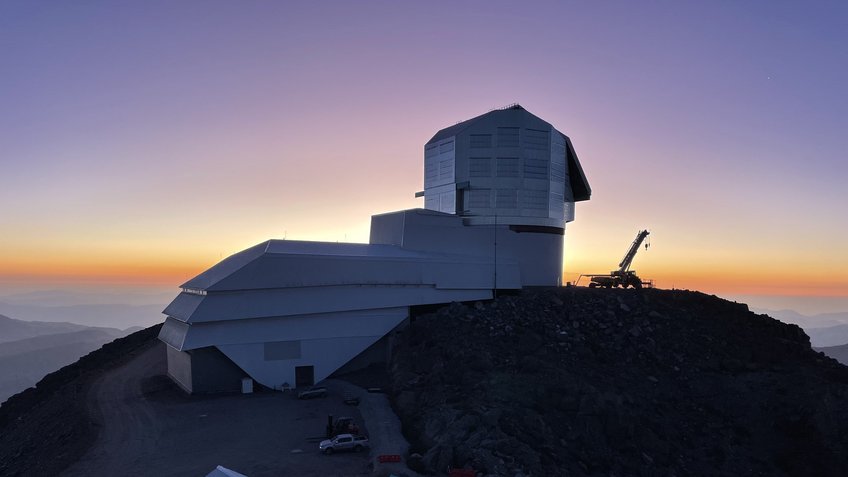 View of Vera C. Rubin Observatory beneath the glittering band of the Milky Way. Rubin Observatory, located in Chile, will use an 8.4-meter telescope equipped with the largest digital camera in the world to conduct a 10-year survey of the entire southern hemisphere sky beginning in late 2025. Large observatory on a mountain at sunset.