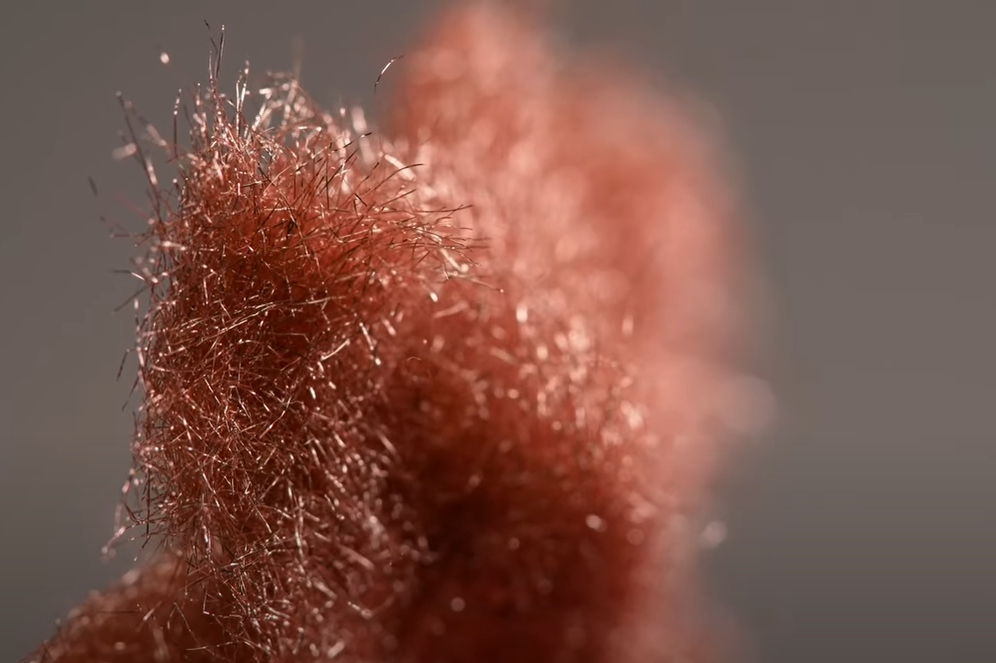 Close-up along the length of a fleece made of fine copper fibres. The metal fibres are sharp in the foreground and become blurred towards the back.