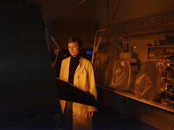 Martina Preiner steht vor Instrumenten im Labor des Max-Planck-Instituts für terrestrische Mikrobiologie, die Plastikhauben vor Staub schützen. Mit diesen untersucht sie sonst die brodelnde Chemie der frühen Erde. Frau mit Schutzkleidung, umgeben von Geräten in einem Chemielabor.