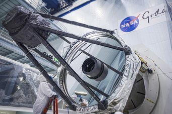 Ein Optikingenieur führt eine Inspektion des Hauptspiegels des Roman-Weltraumteleskops durch. Dieser hat, genau wie der Spiegel des Hubble-Weltraumteleskops, einen Durchmesser von 2,4 Metern. Großer Spiegelteleskop im Reinraum mit NASA-Logo im Hintergrund.
