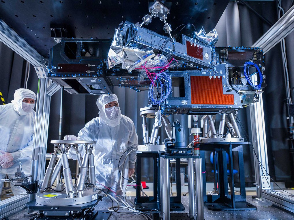 Laborumgebung mit zwei Personen in Schutzanzügen und komplexer technischer Ausrüstung.